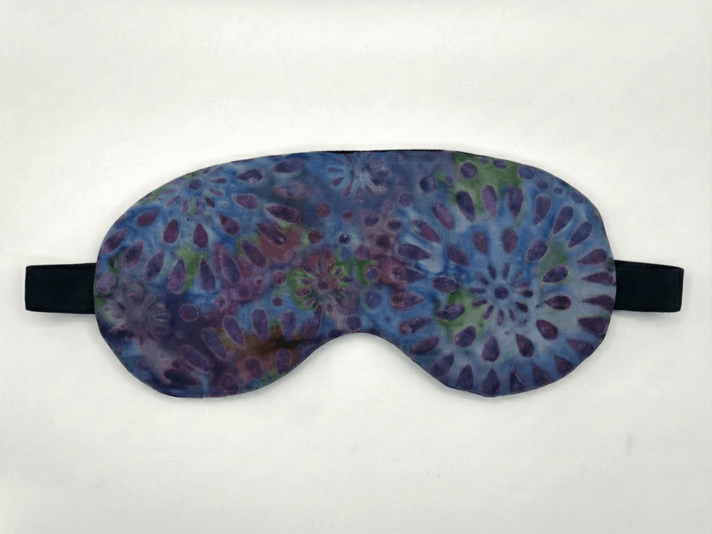 a lavender eye mask. the eye mask has a purple floral tie-die pattern on it, is hand sewn, and has an elastic strap. the eye mask is filled with lavender buds has a subtle natural fragrance.