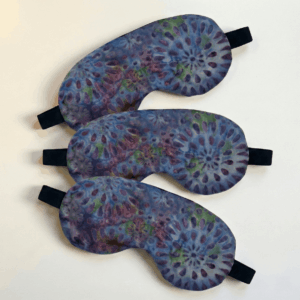 a lavender eye mask three pack. each eye mask has a purple floral tie-die pattern on it, is hand sewn, and has an elastic strap. the eye mask is filled with lavender buds has a subtle natural fragrance.
